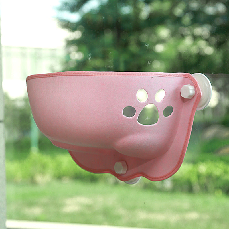 Pink felt cat window pod with paw-shaped cutouts, mounted on clear glass with suction cups, offering a luxury felt cat window pod - designer glass-mounted sun lounger & private hideaway for pets.