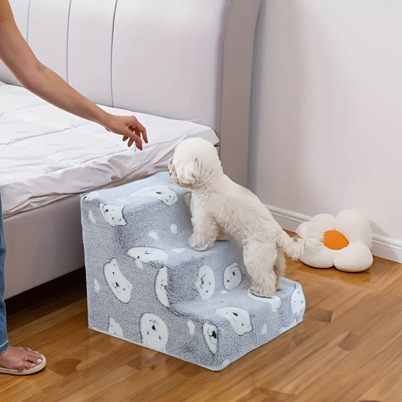 Small white dog climbing gray Tiered High-Density Foam Pet Stairs - Nonslip Pet Steps for High Beds & Sofas - Easy-Access Joint Support with cloud patterns near bed and plush toy on wooden floor.