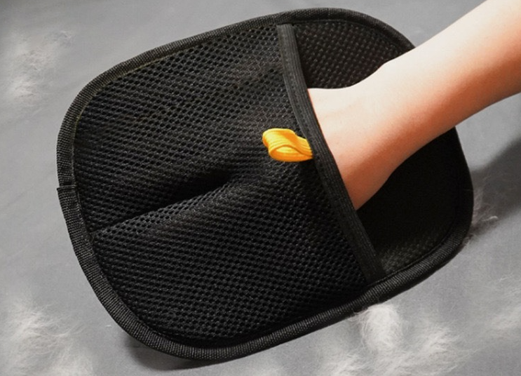 Hand wearing the Electrostatic Pet Hair Removal Glove - Bidirectional Grooming & Fabric Cleaner with a textured black surface and orange pull tab on a smooth gray background.
