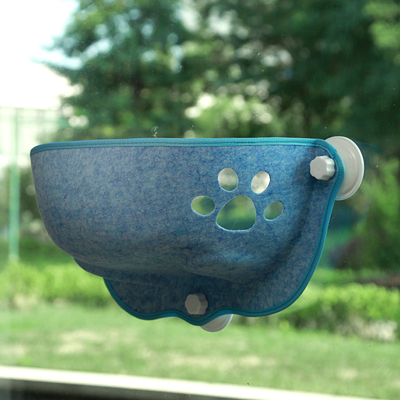 Luxury Felt Cat Window Pod - Designer Glass-Mounted Sun Lounger & Private Hideaway in blue felt with paw print cutout, attached to a window with suction cups, overlooking a backyard garden.