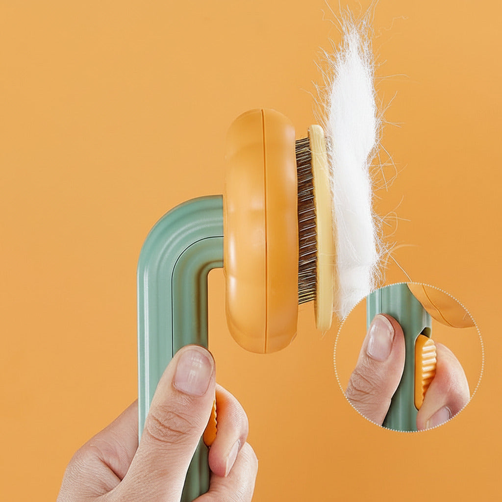Hand holding Boutique Pumpkin Self-Cleaning Brush - Aesthetic Grooming & Deshedding Comb with white pet hair being released from bristles by pressing a thumb button on a green and orange handle against a solid orange background.