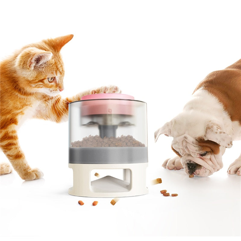Orange tabby cat pawing at the Gravity Catapult Puzzle Feeder - Interactive IQ Training & Slow Feed Station as a bulldog eats scattered kibble nearby on a white background