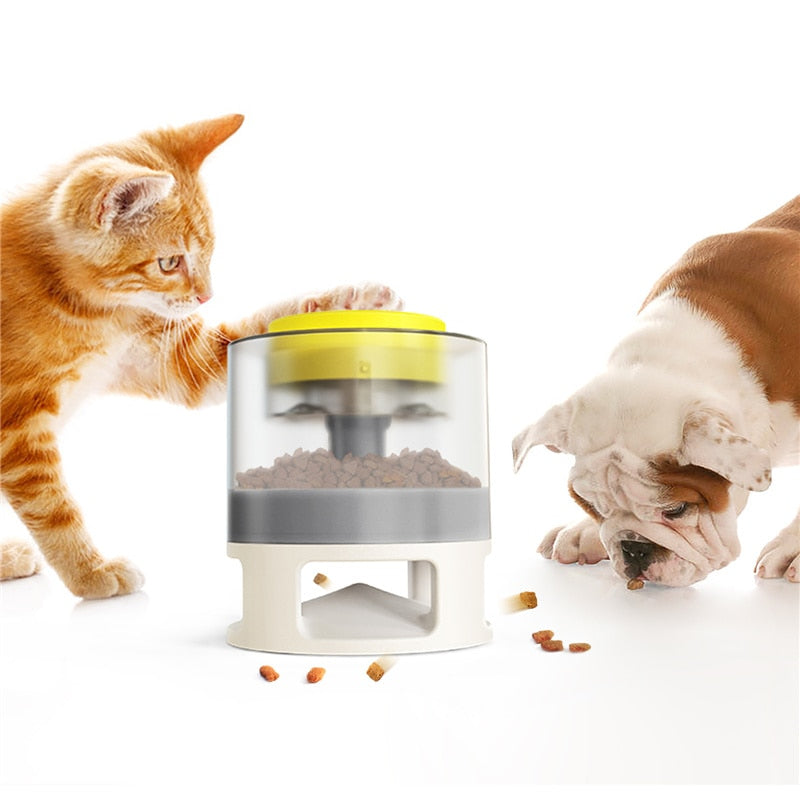An orange tabby cat interacts with the Gravity Catapult Puzzle Feeder - Interactive IQ Training & Slow Feed Station while a bulldog eats kibble from the floor nearby, demonstrating the feeder’s engaging and slow feeding design.