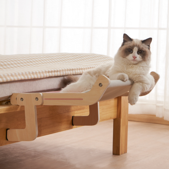 A relaxed cat lounging on a No-Suction Wooden Cat Window Perch - Heavy-Duty Adjustable Hook-On Shelf & Safety Sun Lounger attached to a wooden bed frame near a window with soft natural light.