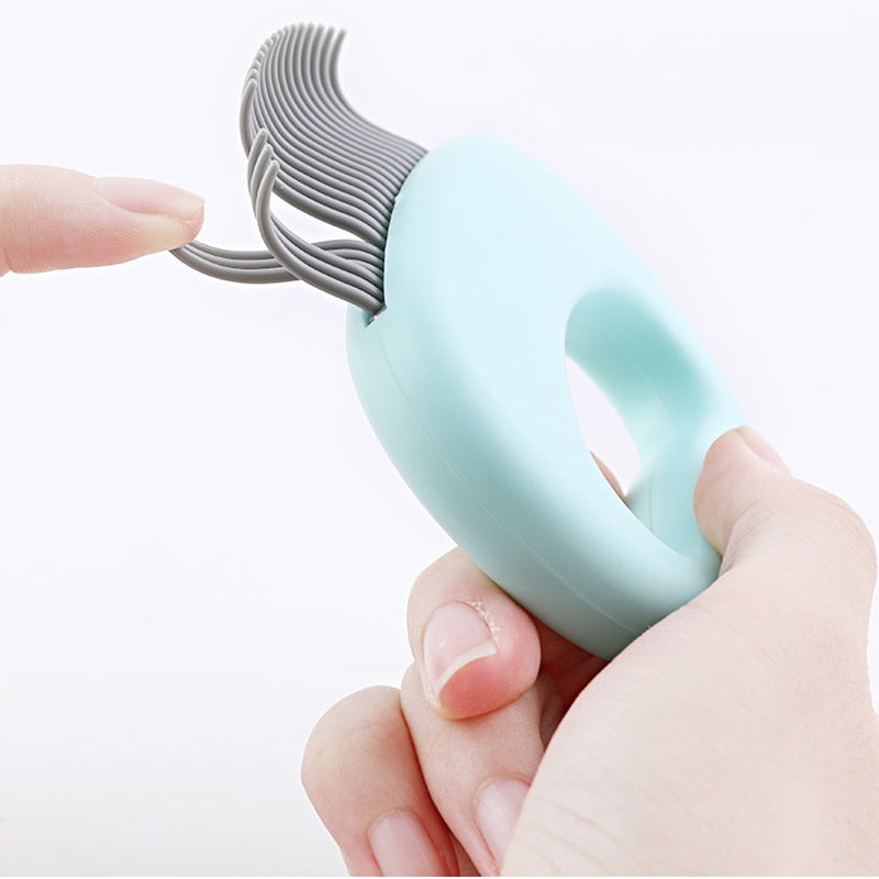 Hand holding a light blue Feline Shell Massage Comb - Whisker-Friendly Soft-Needle Deshedding Tool, showing flexible soft needles bending gently between fingers.