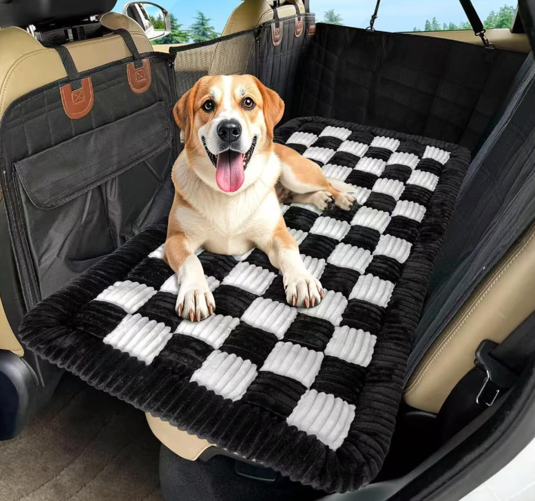Happy dog lying on a black and white checkered mat in the backseat of a car showcasing the Designer Checkered Travel Dog Bed - Thickened Quilted Car Seat Mat - Nonslip Portable Pet Sleeping Pad.