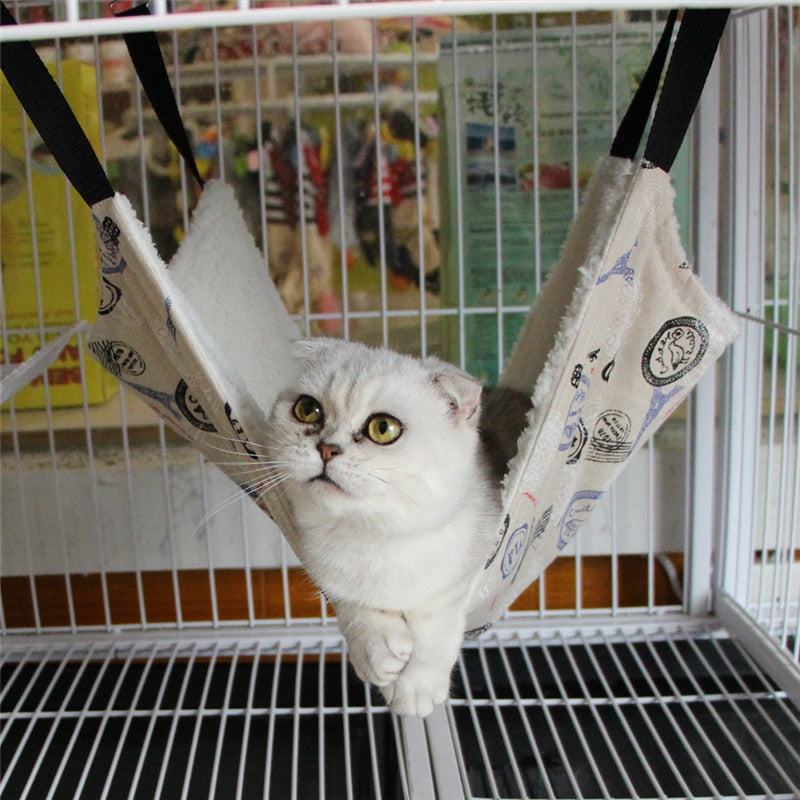 White cat comfortably resting in a Thermal Hanging Cat Hammock - Double-Sided Winter Warm Fleece Bed for Cages, Crates & Chairs, suspended inside a metal cage.