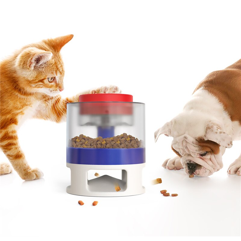 Orange tabby cat pawing at the Gravity Catapult Puzzle Feeder - Interactive IQ Training & Slow Feed Station while a bulldog eats kibble from the base on a white background.