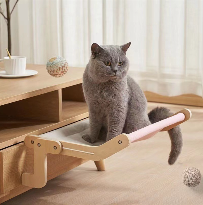 A gray cat sitting comfortably on a light wooden No-Suction Wooden Cat Window Perch - Heavy-Duty Adjustable Hook-On Shelf & Safety Sun Lounger attached to a wooden cabinet with soft cushions around.