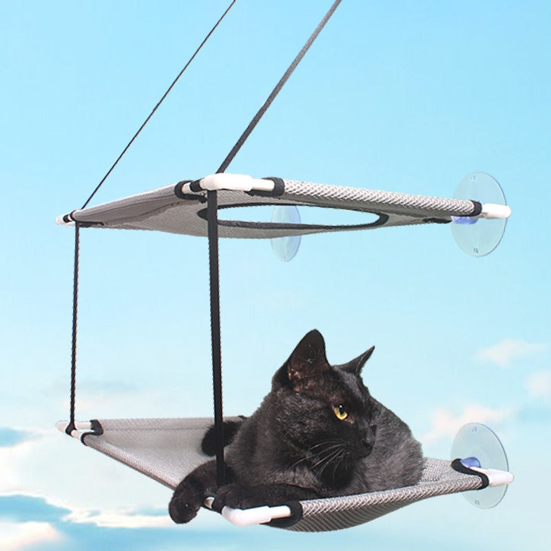 A black cat resting comfortably on the Double-Decker Cat Window Hammock - Multi-Level Sun Lounger & Space-Saving Glass-Mounted Perch attached to a window with suction cups against a clear blue sky.