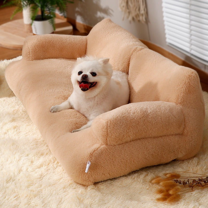 Small white dog resting contentedly on a beige Orthopedic Calming Pet Sofa - Luxury Plush Dog & Cat Bed Couch with Bolster Support placed on a soft cream rug in a cozy room setting.