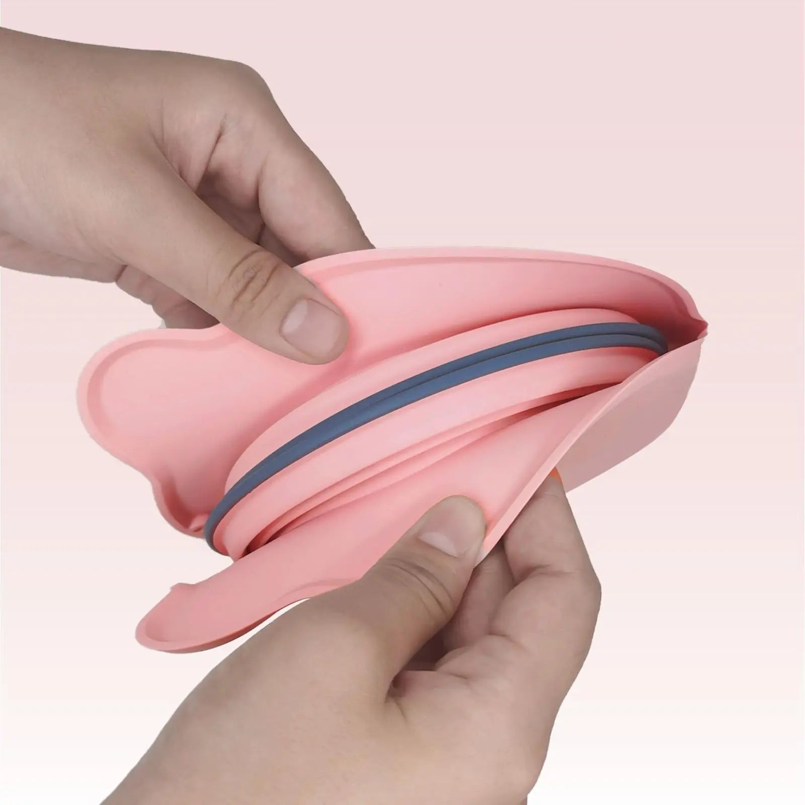 Hands folding a pink and gray flexible silicone bowl designed as the 2-in-1 Collapsible Travel Slow Feeder - Portable Hydration & Feeding Station for easy storage and travel.
