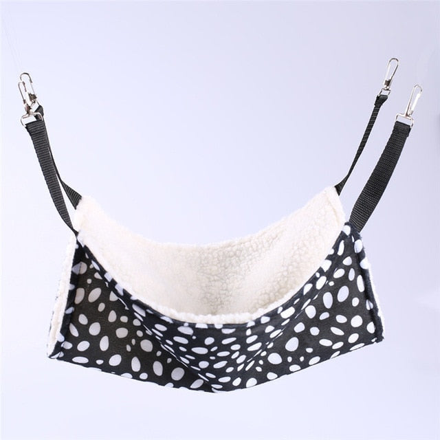 Thermal Hanging Cat Hammock - Double-Sided Winter Warm Fleece Bed for Cages, Crates & Chairs with black and white spotted exterior and soft cream fleece interior suspended by adjustable straps and metal clips.